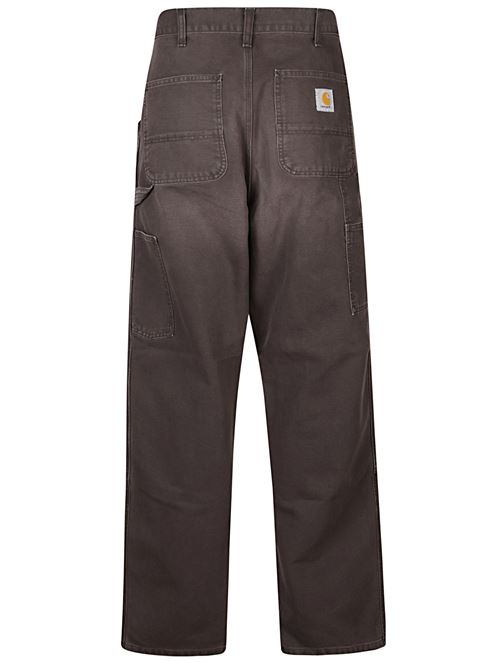 Pantalone marrone di CARHARTT WIP caratterizzato da vita media con passanti per cintura, tasche frontali con dettagli in metallo e cuciture rinforzate sulle ginocchia. CARHARTT WIP | I034796474O